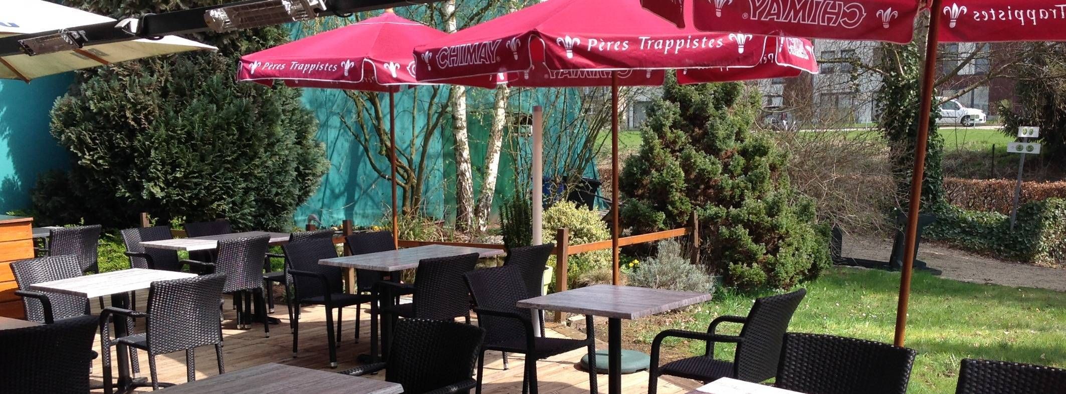 La terrasse du Longchamps en été : tables, parasols rouges et jardin le long des courts