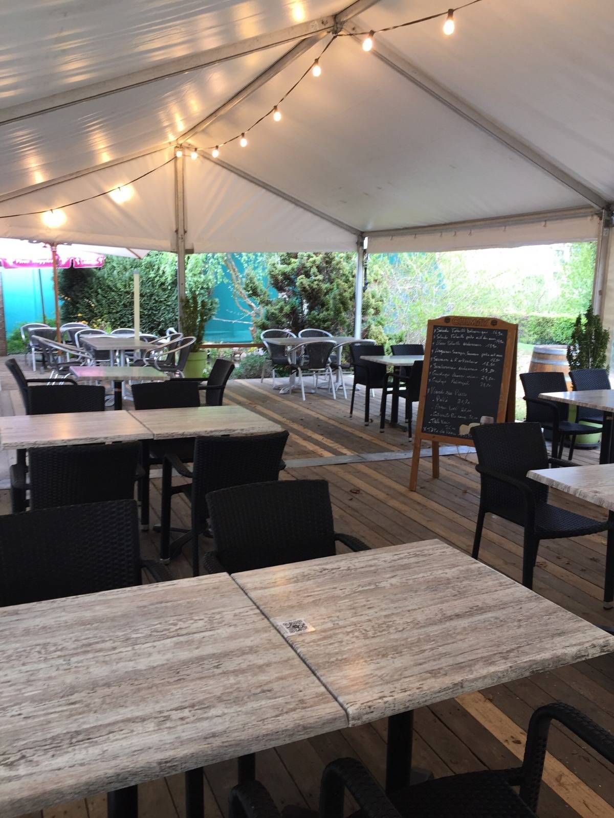 La terrasse couverte sous sa toile, guirlandes lumineuses et tables en bois