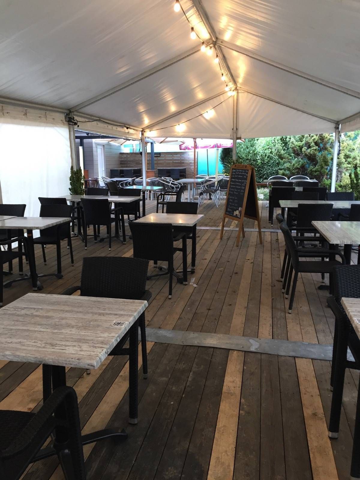 La terrasse couverte sous sa toile, guirlandes et tables en bois